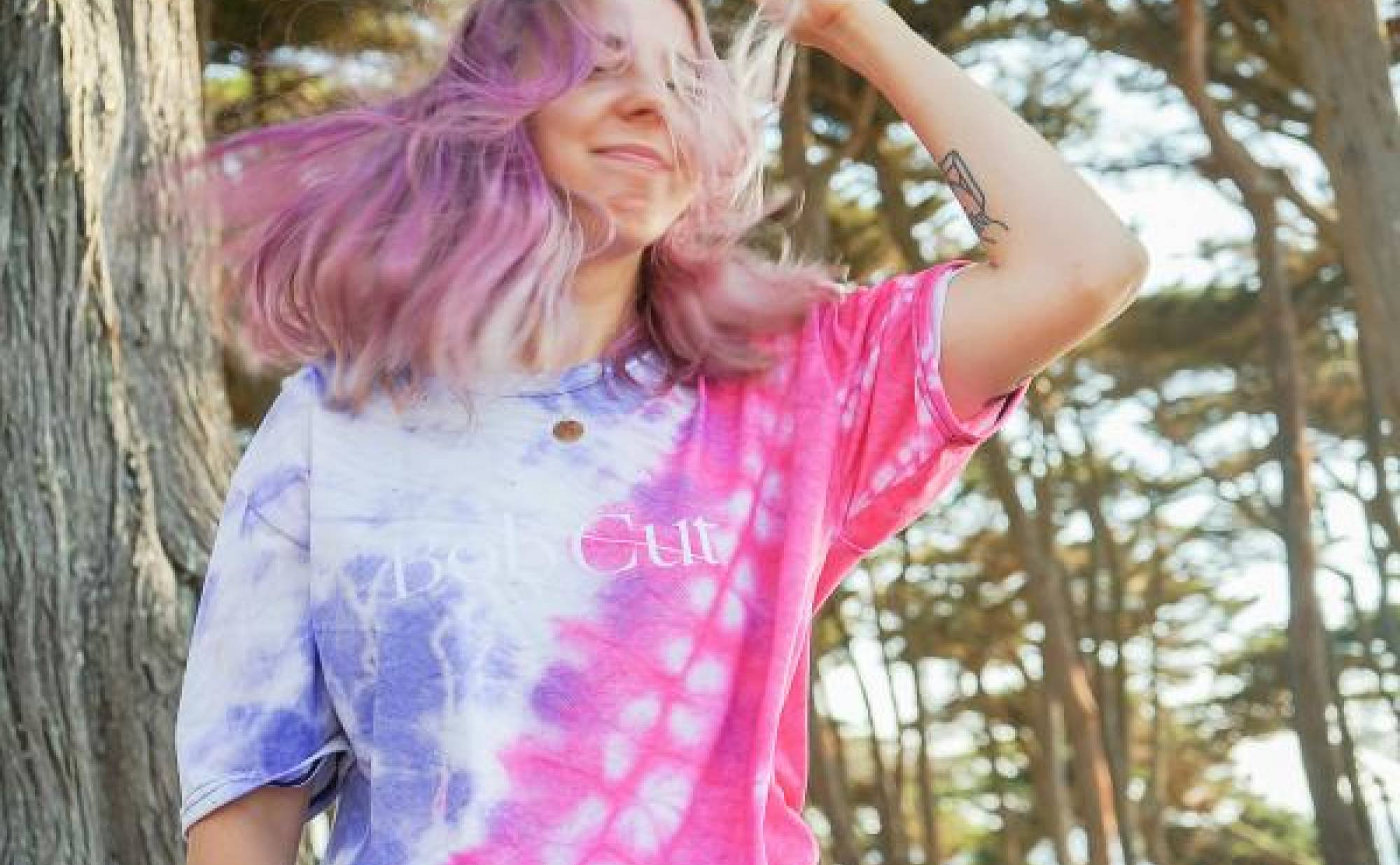 A young person with pink hair wearing a tie dye shirt. 