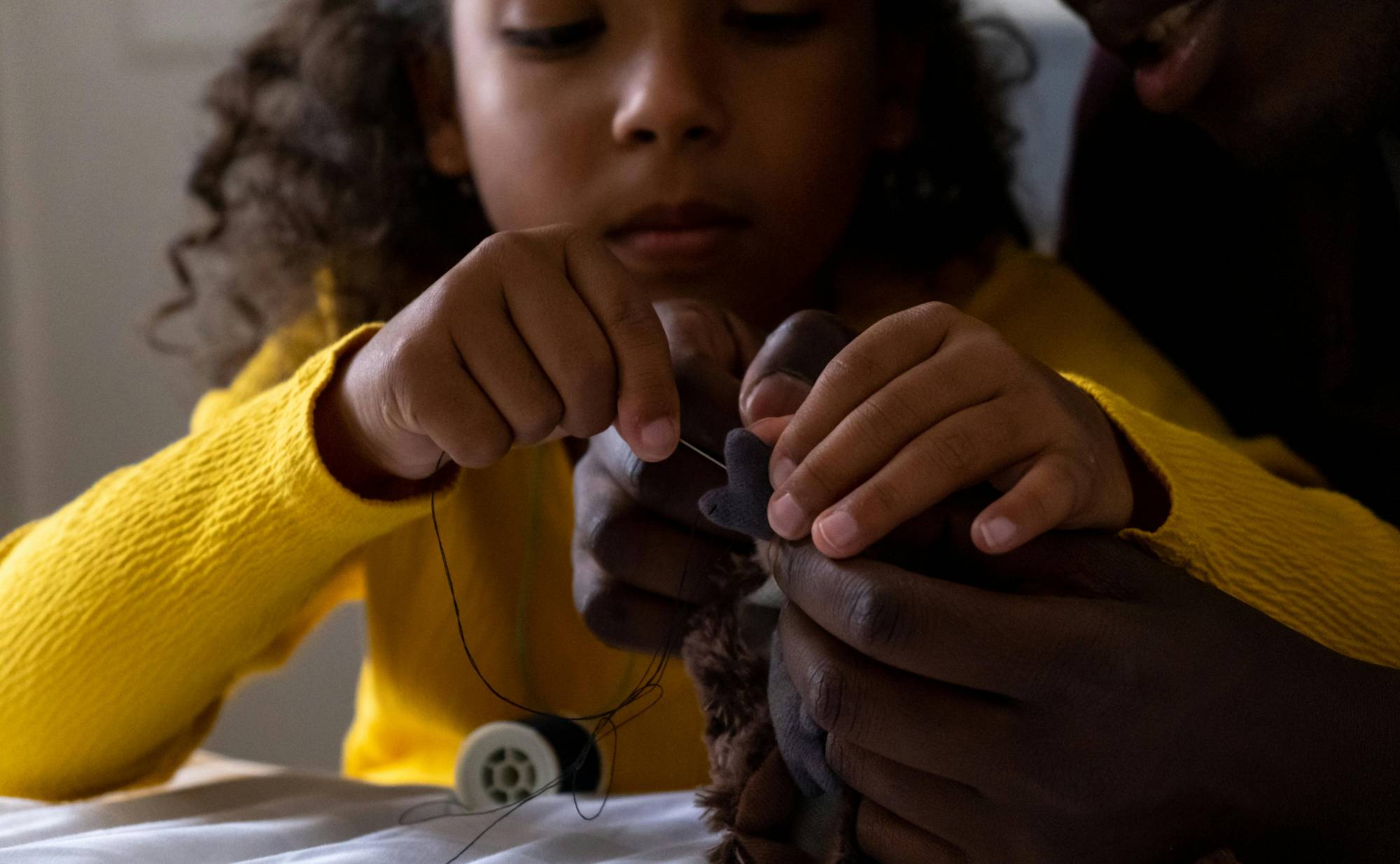 Child sewing a stuffed animal with an adult.