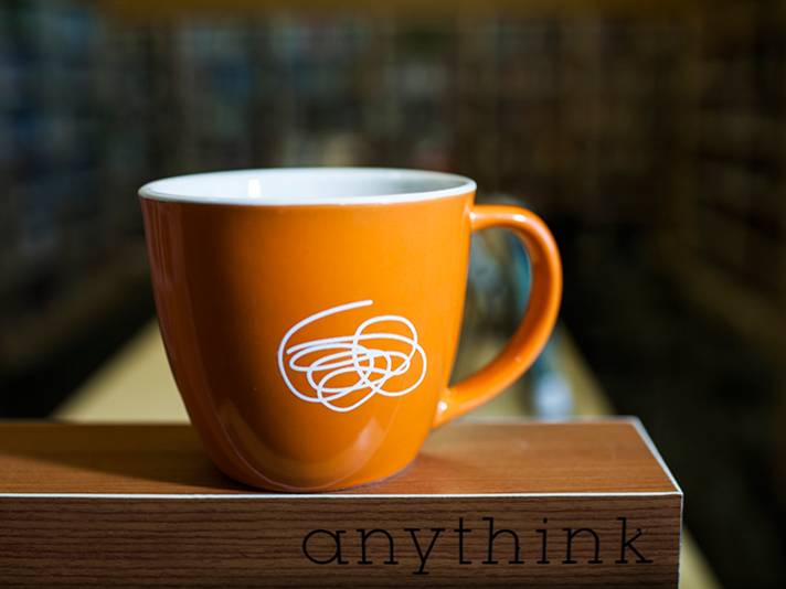 A orange mug with white Anythink doodle.